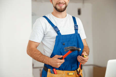Cropped shot of professional handyman worker in uniform smiling at camera and holding hammer during renovation work indoorsの写真素材