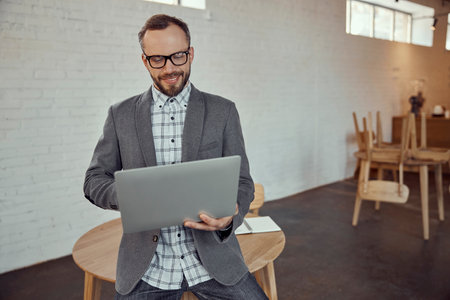 Joyful bearded man using laptop in cafeの写真素材