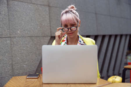 Female straightening glasses while looking at laptop screen outdoorsの写真素材