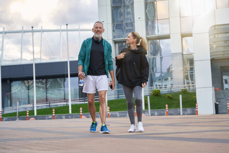 Full length shot of sportive middle aged couple in sportswear looking cheerful while walking together outdoors after workoutの写真素材