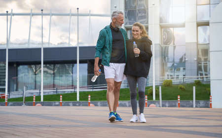 Full length shot of active middle aged couple in sportswear looking cheerful while walking together outdoors after gym workoutの写真素材