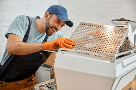 Cheerful male worker fixing coffee machine in cafeの写真素材