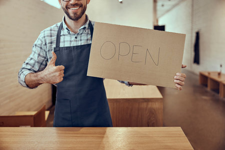 Joyful man holding open sign and giving thumbs upの写真素材