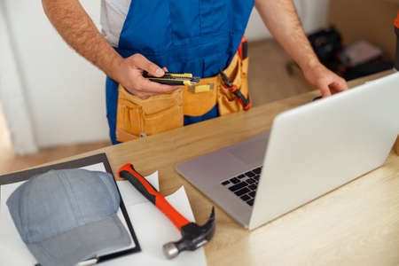 Cropped shot of repairman worker in uniform wearing tool belt, holding utitlity knife and using...