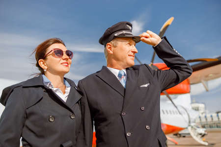 Joyful aircraft pilot and stewardess standing outdoors at airportの写真素材