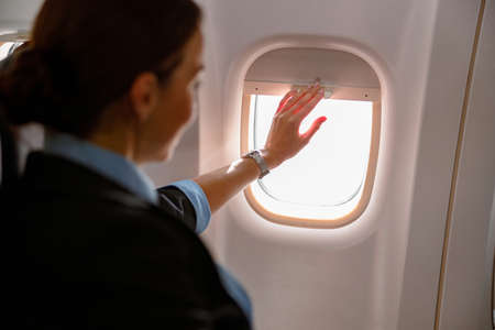Female flight attendant closing window in aircraftの写真素材