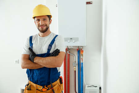 Smiling technician servicing the house heating system looking at camera while standing with arms crossedの写真素材