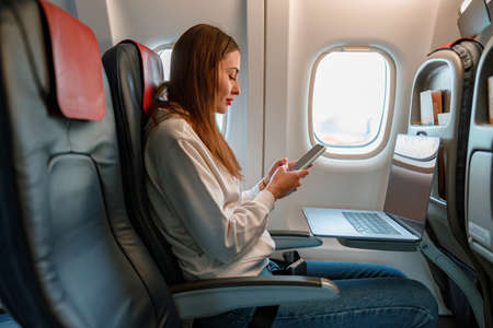 Young woman using laptop and cellphone in airplane