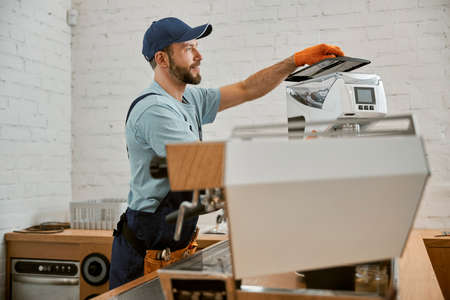 Smiling man repairing coffee machine in cafeの写真素材