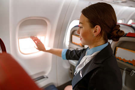 Female flight attendant closing window in airplaneの写真素材