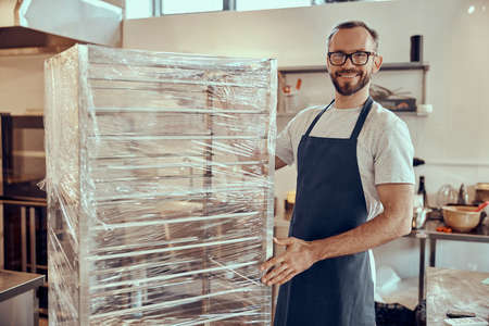 Cheerful male worker standing by showcase in cafe