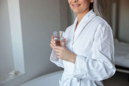 Close-up of lady in bathrobe with glass of waterの写真素材