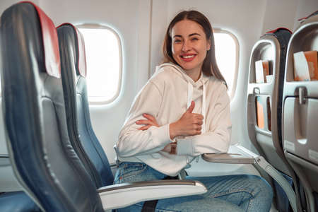 Joyful young woman doing thumbs up gesture in airplaneの写真素材