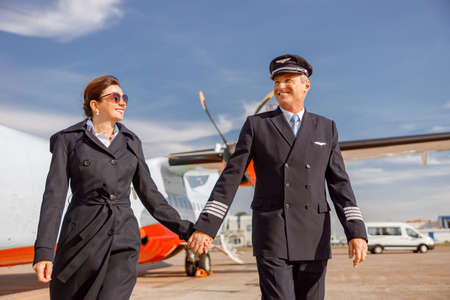 Joyful male pilot and his wife waking hand in hand at airportの写真素材