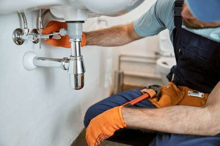 Male plumber hands repairing pipe under sinkの写真素材