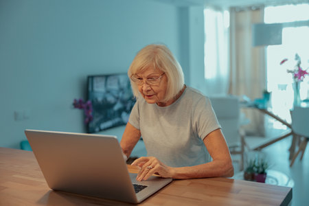 Senior woman communicating during video chat on laptop indoorsの写真素材