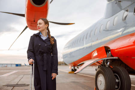 Cheerful woman standing near passenger airplane at airportの写真素材