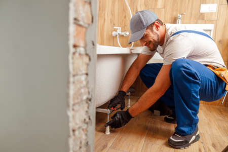 Cheerful plumber or technician preparing details for bathtub installation in bathroomの写真素材