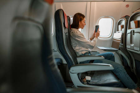 Young woman taking photo with cellphone in airplaneの写真素材