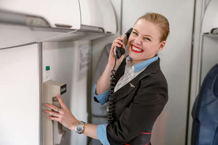 Cheerful flight attendant talking on telephone in airplane cabinの写真素材