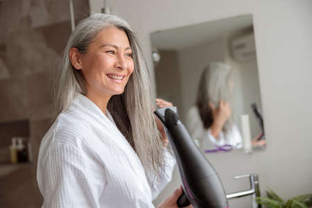 Woman styling hair after taking a bath at homeの写真素材