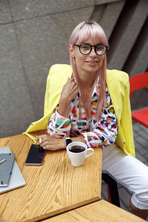 Woman in yellow jacket in street cafe staring at cameraの写真素材