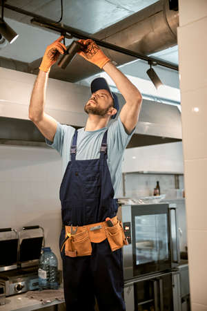 Male worker fixing ceiling lamp in cafeの写真素材
