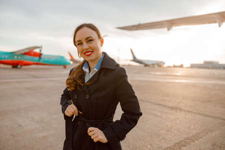Cheerful woman tying coat belt at airportの写真素材