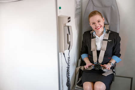 Cheerful female flight attendant sitting in chair in airplaneの写真素材