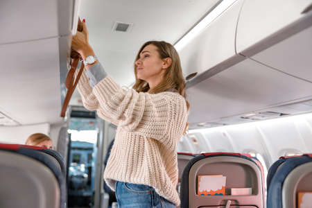 Young woman putting travel bag in cabin compartmentの写真素材