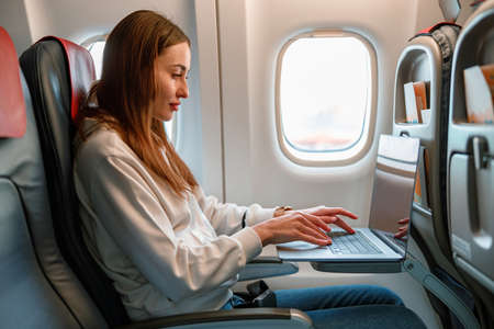 Young woman using laptop in passenger airplaneの写真素材