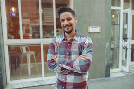 Portrait of happy man in plaid shirt standing near cafeの写真素材