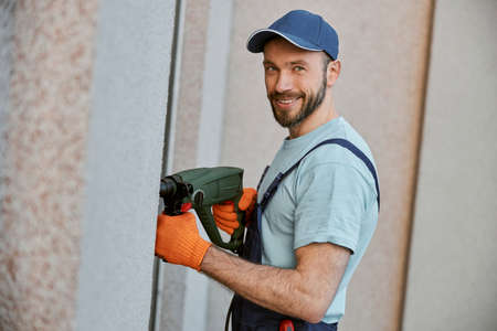Cheerful male builder drilling wall with electric drillの写真素材