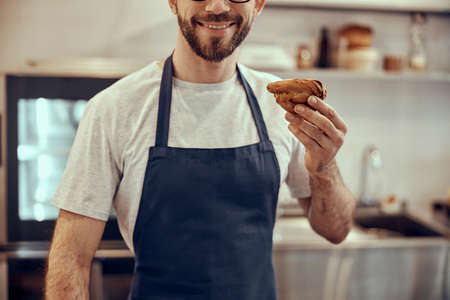 Cheerful male worker in apron holding pastryの写真素材