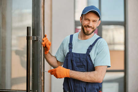 Cheerful young man repairing door in buildingの写真素材