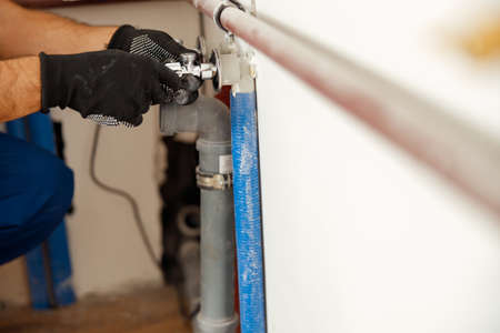 Closeup of hands of plumber checking pipes while installing heating system in apartmentの写真素材