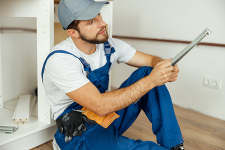 Busy male worker in overalls assembling kitchen furniture, sitting on the floorの写真素材