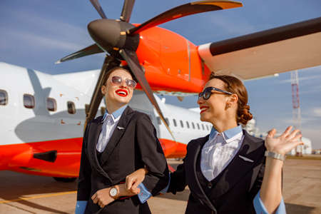 Cheerful women stewardesses walking arm in arm at airportの写真素材