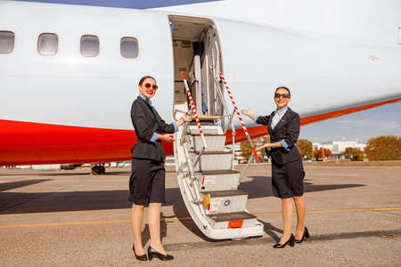 Cheerful stewardess standing near airplane and inviting on boardの写真素材
