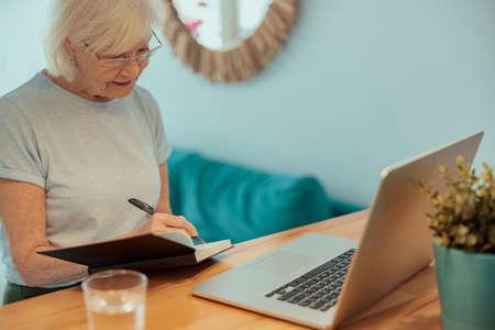 Beautiful older lady taking notes at homeの写真素材