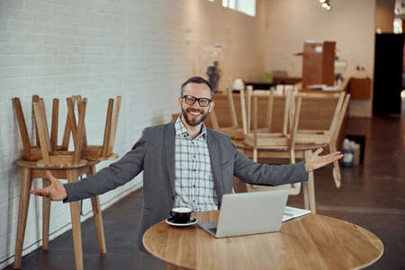 Cheerful man sitting at the table and using laptop in cafeの写真素材