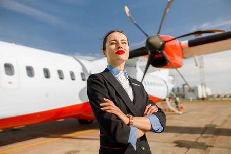 Female airline worker standing near plane at airportの写真素材