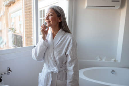 Asian lady doing face clean standing near the window in bathroomの写真素材