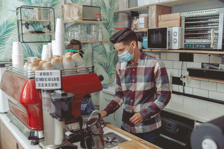 Man barista in protective mask working in cafeの写真素材