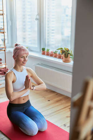 Sportswoman in tracksuit meditates with namaste mudra sitting on knees on balconyの写真素材