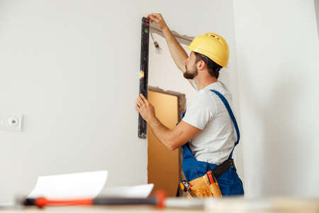 Hard working handyman, builder in uniform measuring the wall using bubble levelの写真素材
