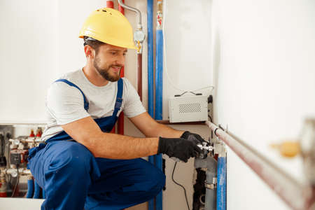 Cheerful male worker, plumber checking pipes while installing heating system in apartmentの写真素材