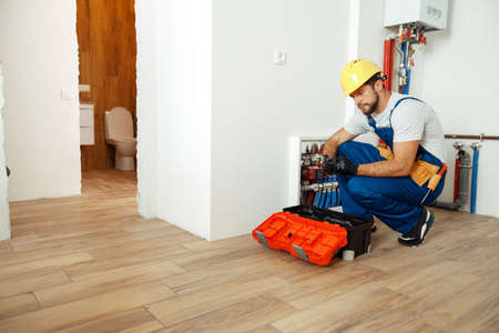 Busy technician, plumber in protective gloves using tools from toolbox while setting water pipesの写真素材