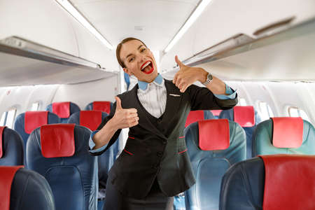 Cheerful woman flight attendant doing thumbs up gesture in planeの写真素材