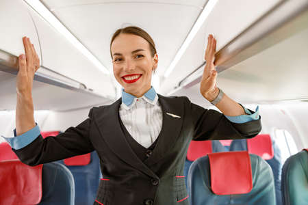 Cheerful woman flight attendant standing in aircraft passenger salonの写真素材